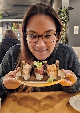 Angelica looking hungrily at a plate of sushi and wearing a grey shirt