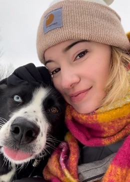 Carla wearing a tuque next to a black and white dog